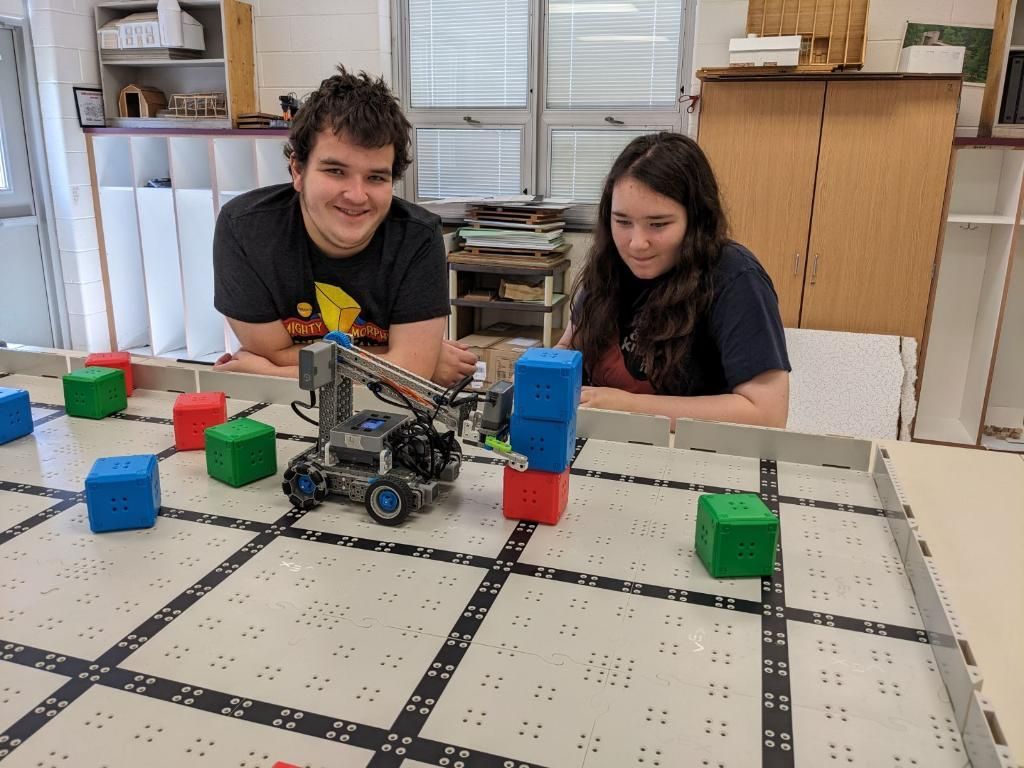 A man and a woman are playing with a robot on a table.