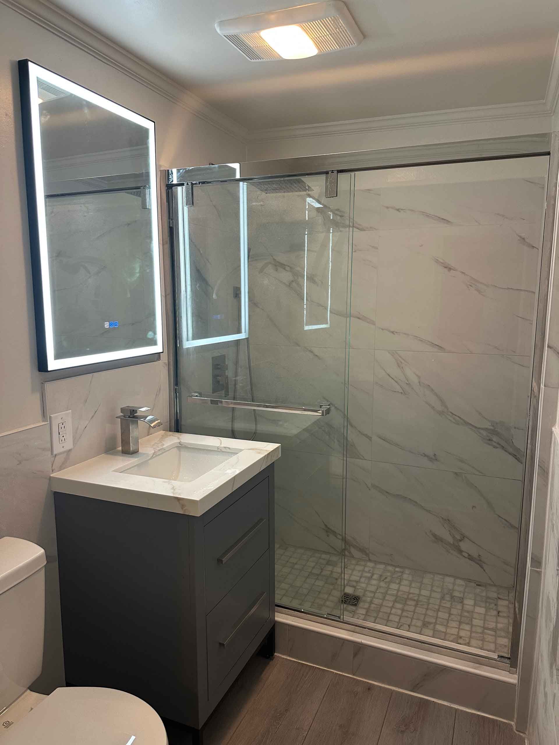 A bathroom with a toilet , sink , mirror and shower.