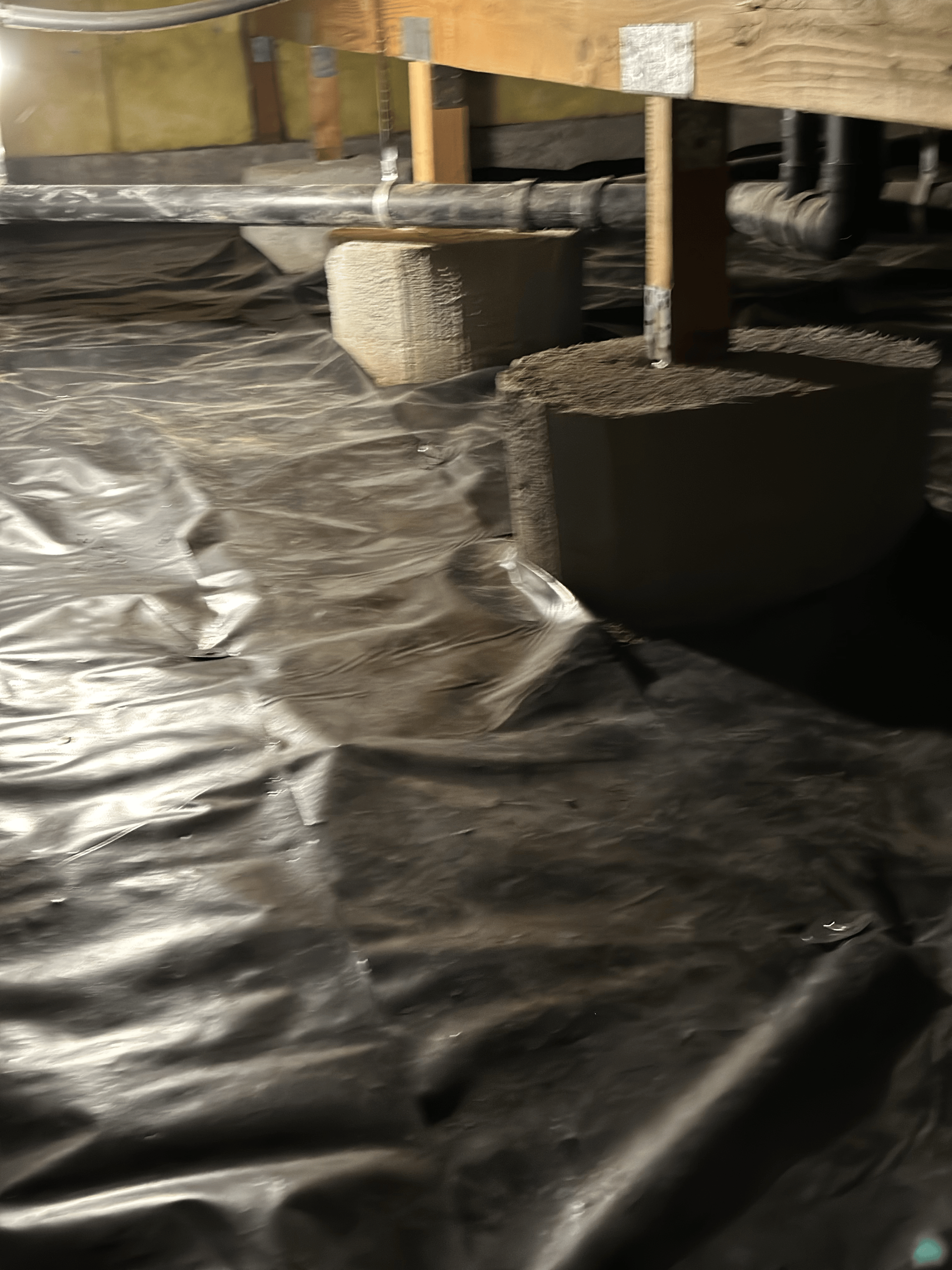A crawl space filled with plastic and concrete blocks.