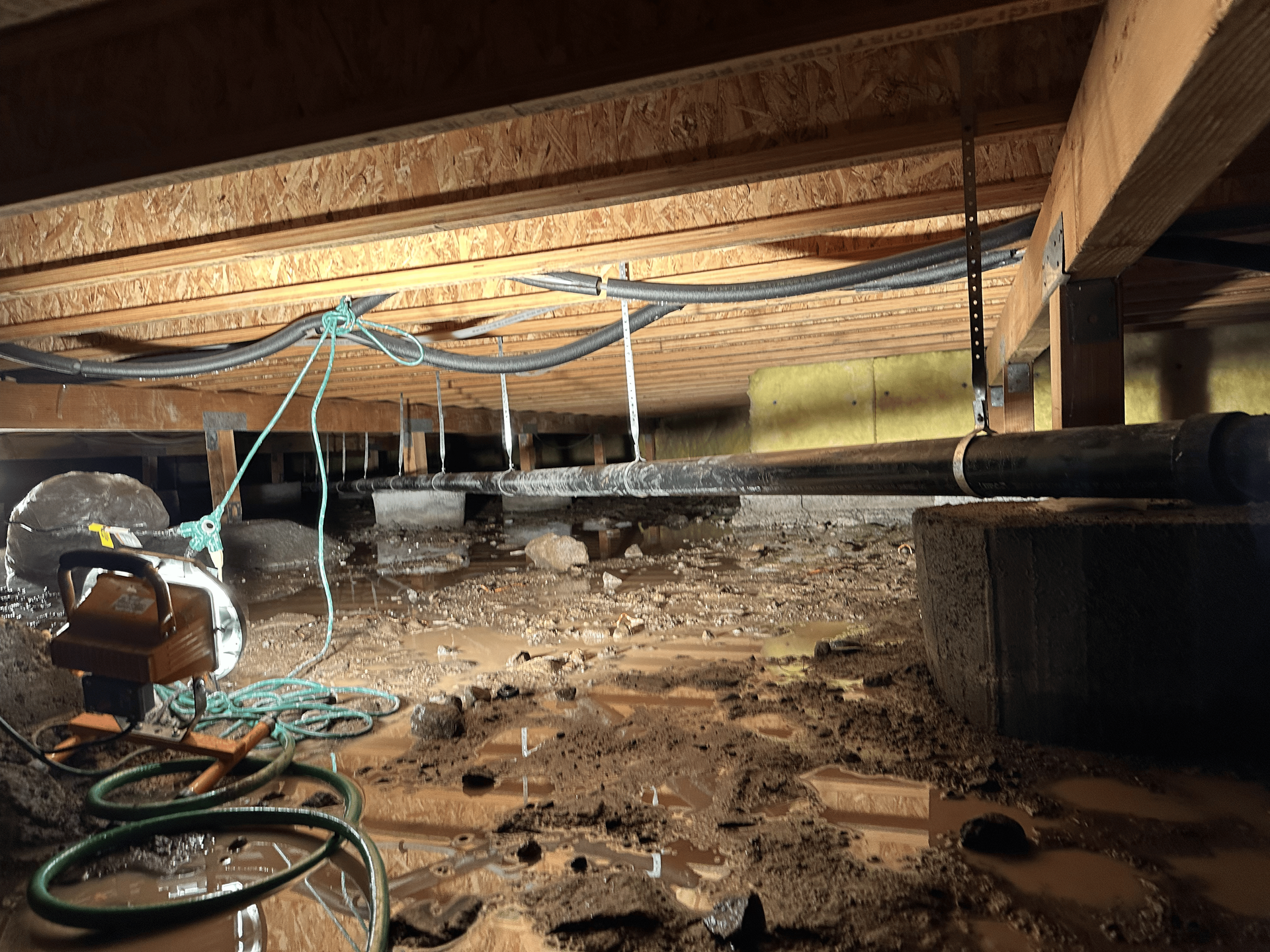 A muddy basement with a fan and a hose.
