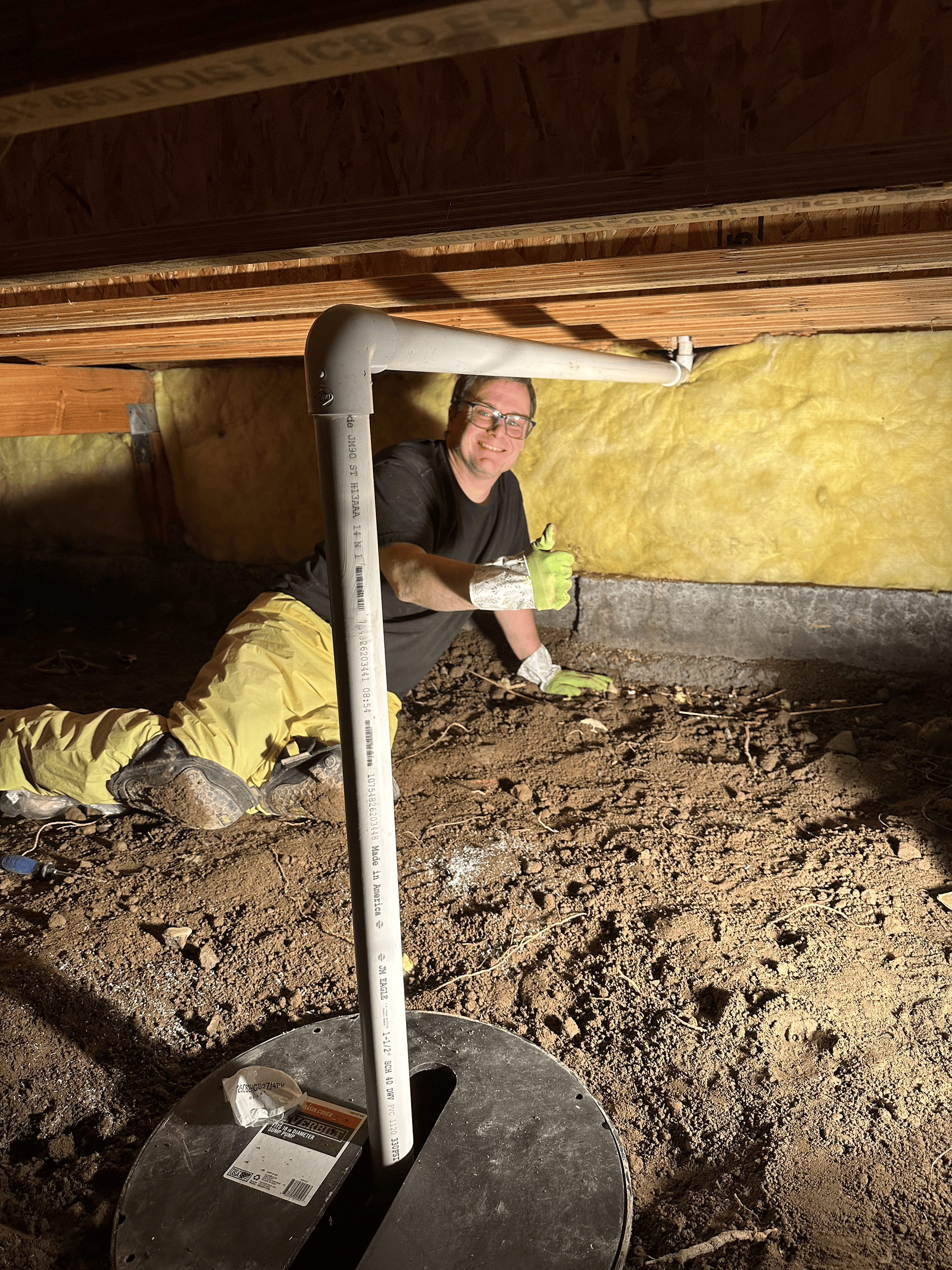 A man is kneeling under a pipe in a basement.