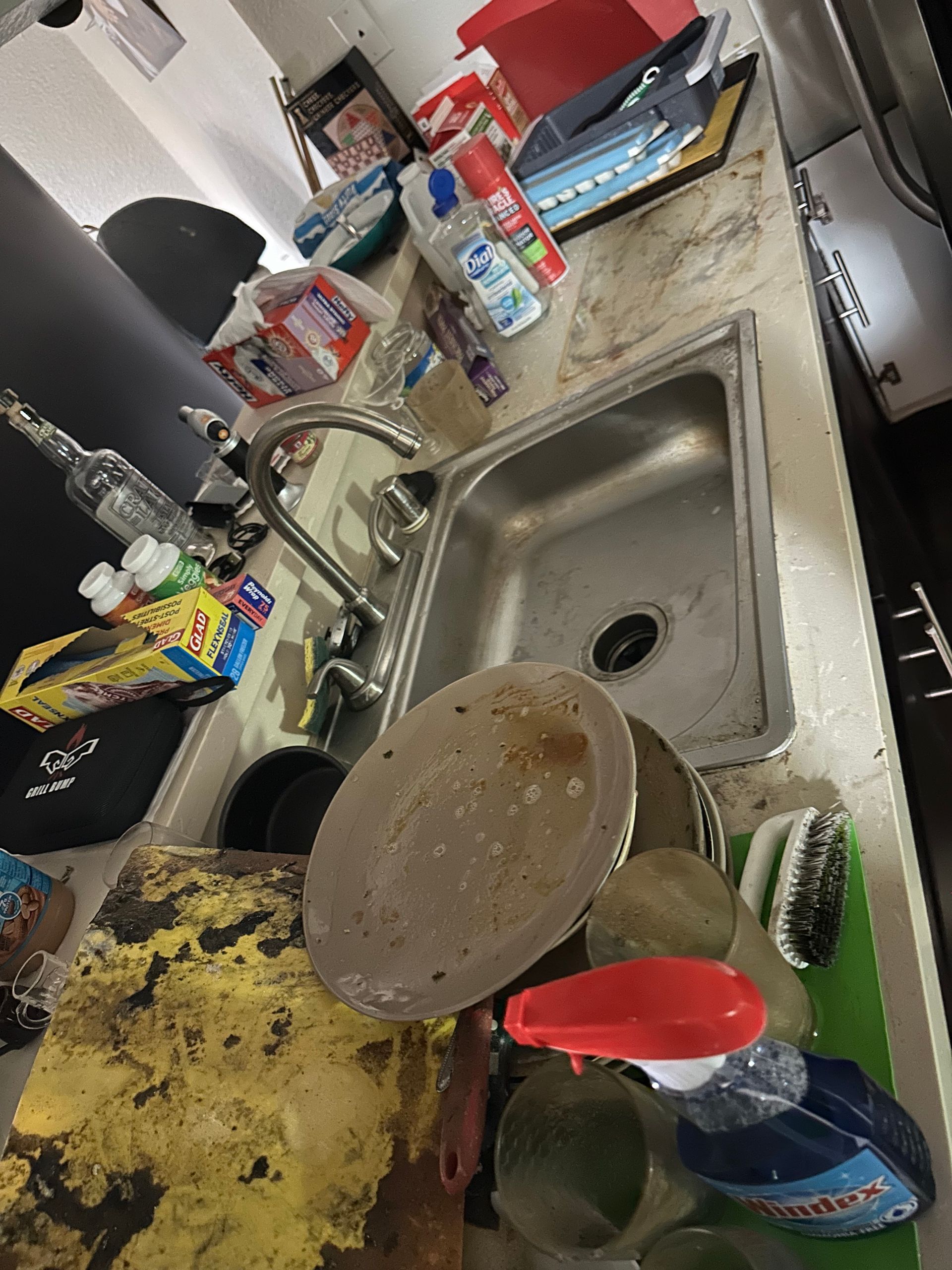 A kitchen counter with a sink , pots and pans , and cleaning supplies.