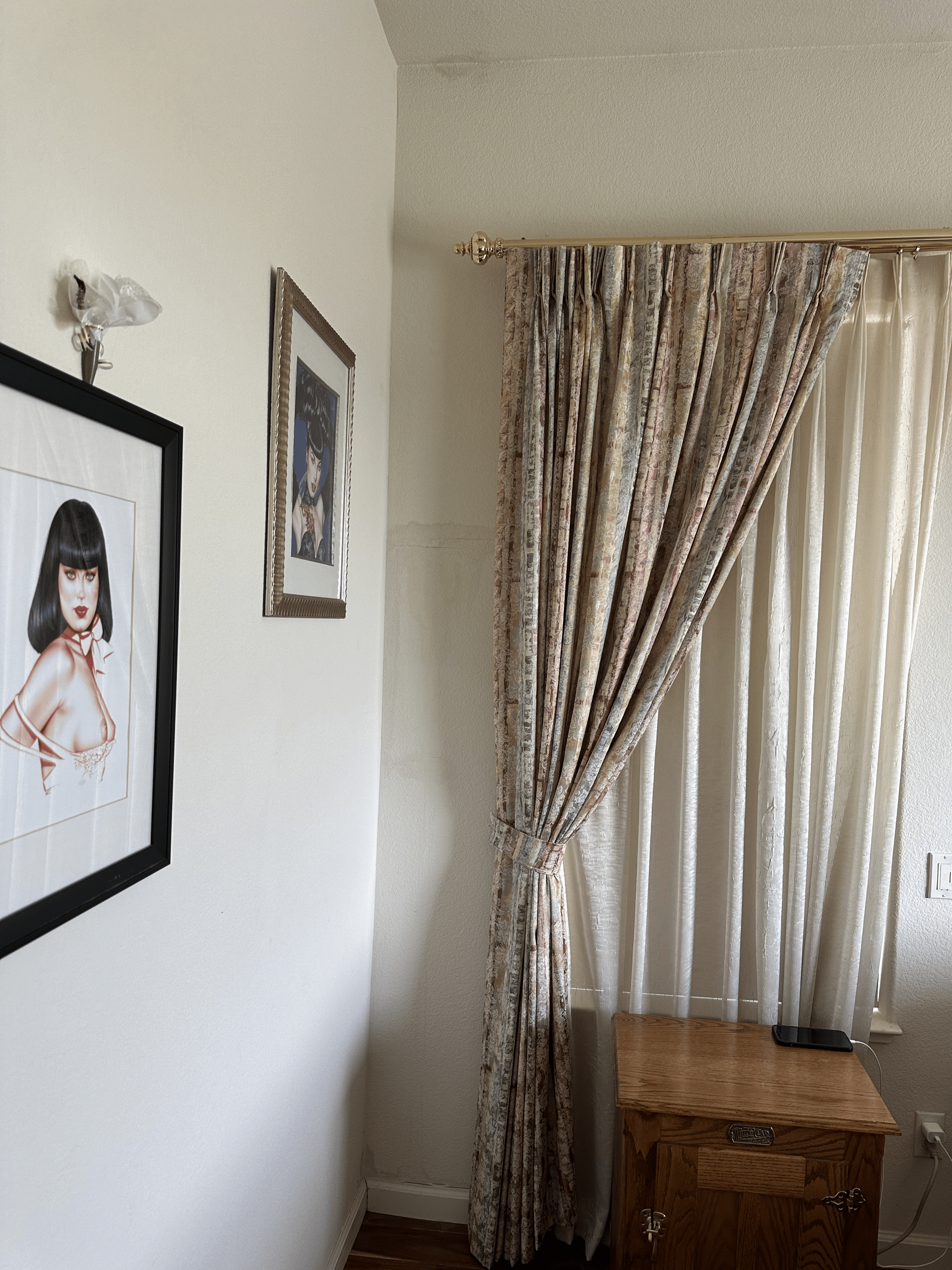 A bedroom with a picture of a woman on the wall and curtains.