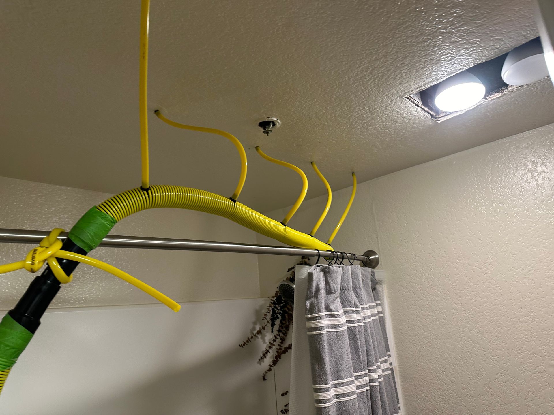 A bathroom with a shower curtain and a yellow hose hanging from the ceiling.