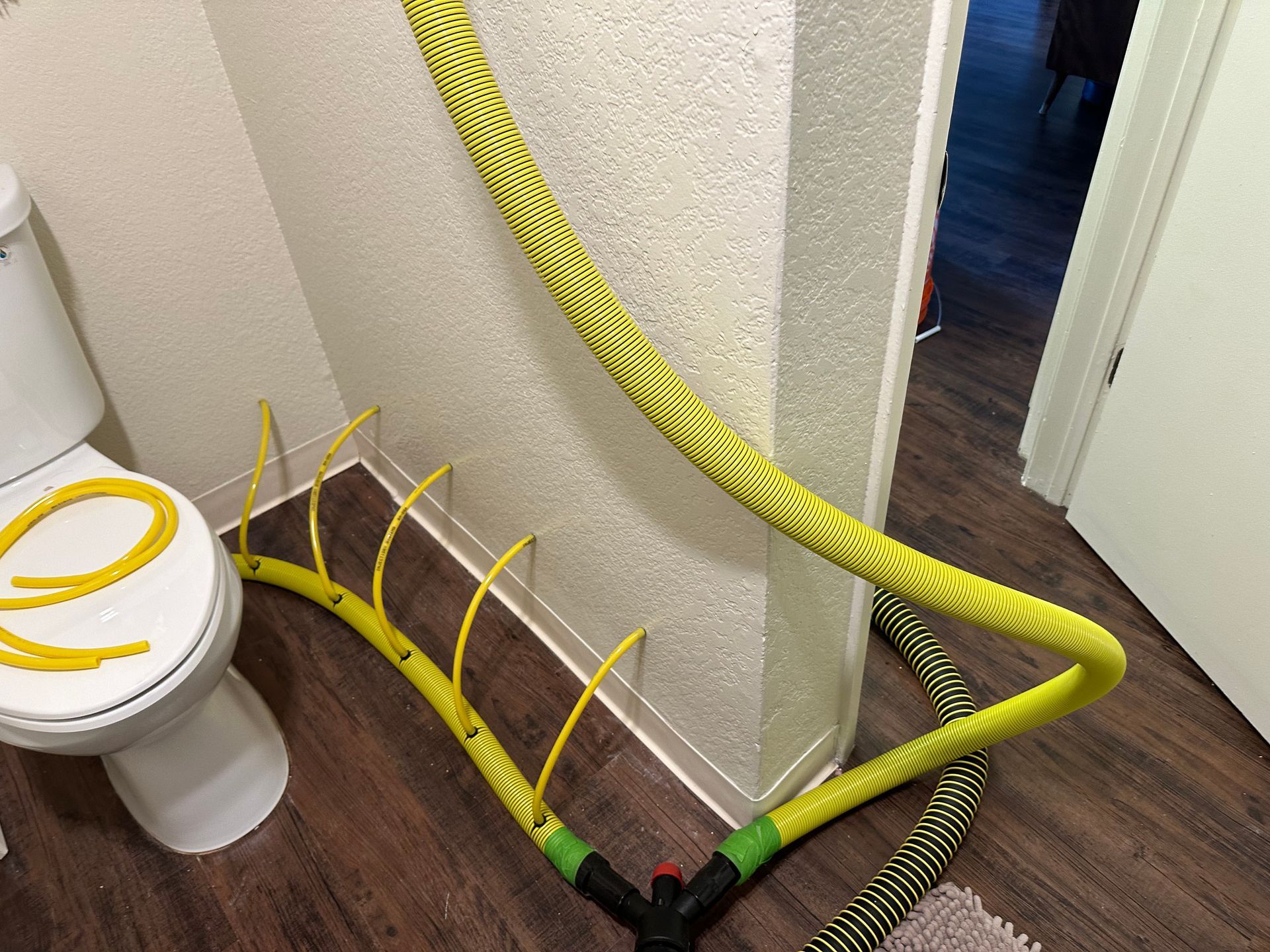 A yellow hose is laying on the floor next to a toilet.