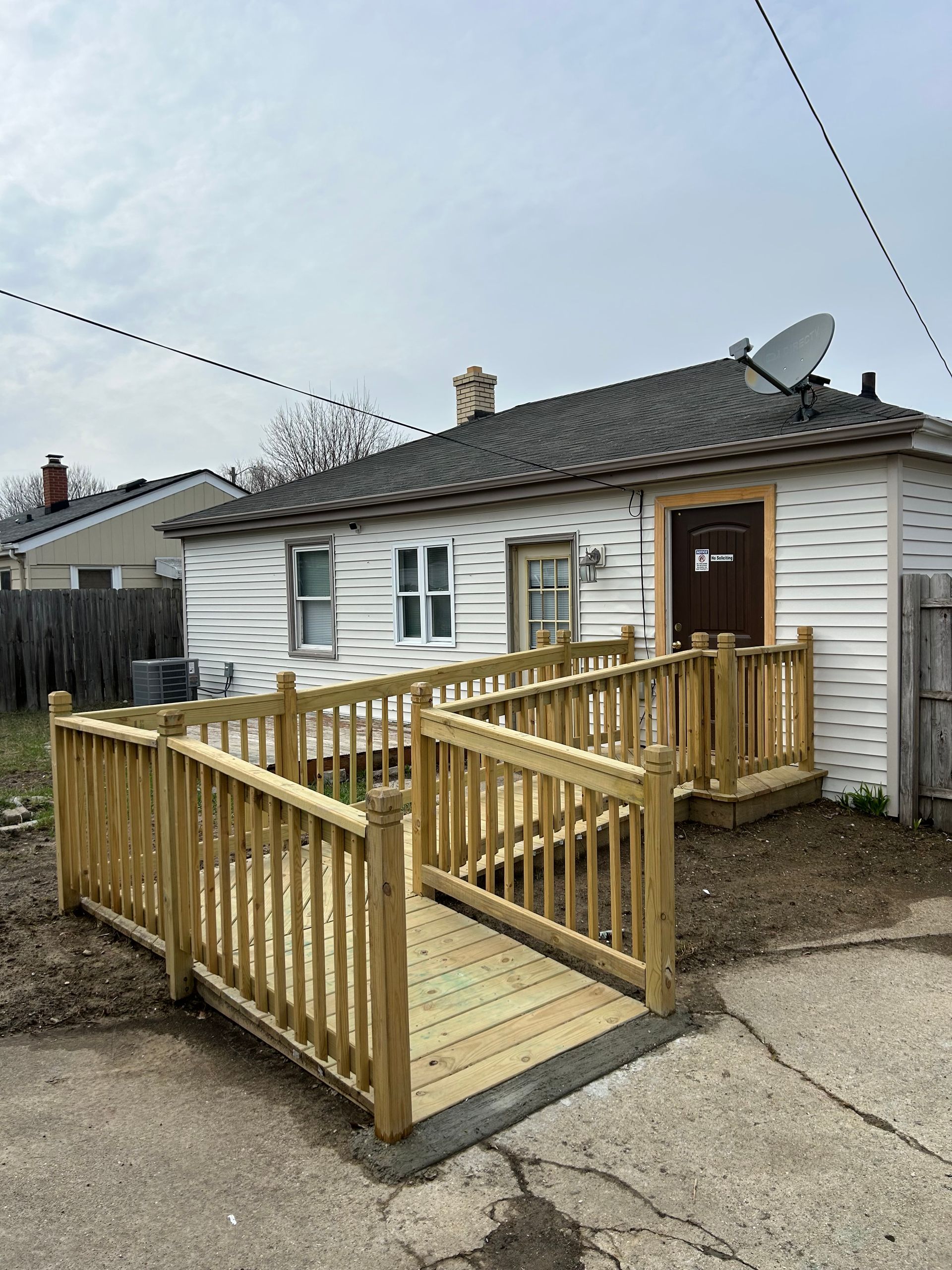 Small house with a wooden accessibility ramp and railing leading to the front door