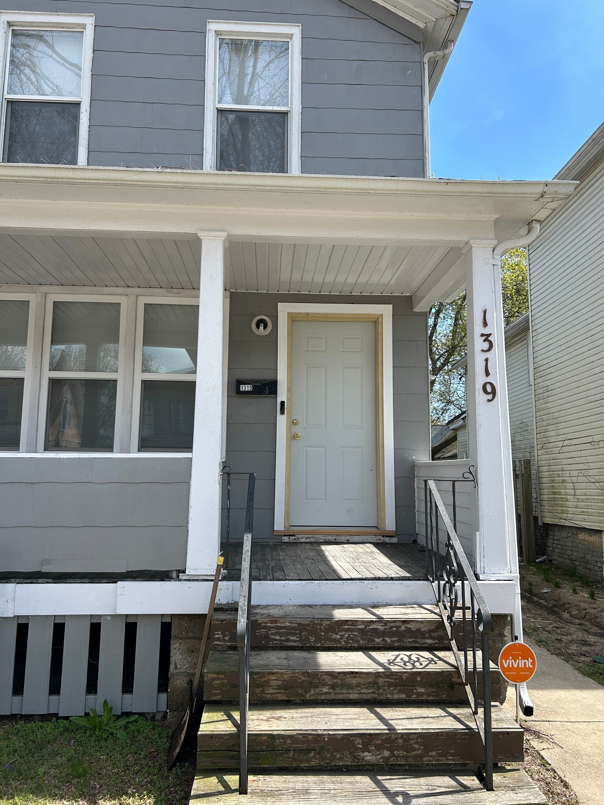 Gray two-story house with front porch, steps, white columns, and numbered pillar