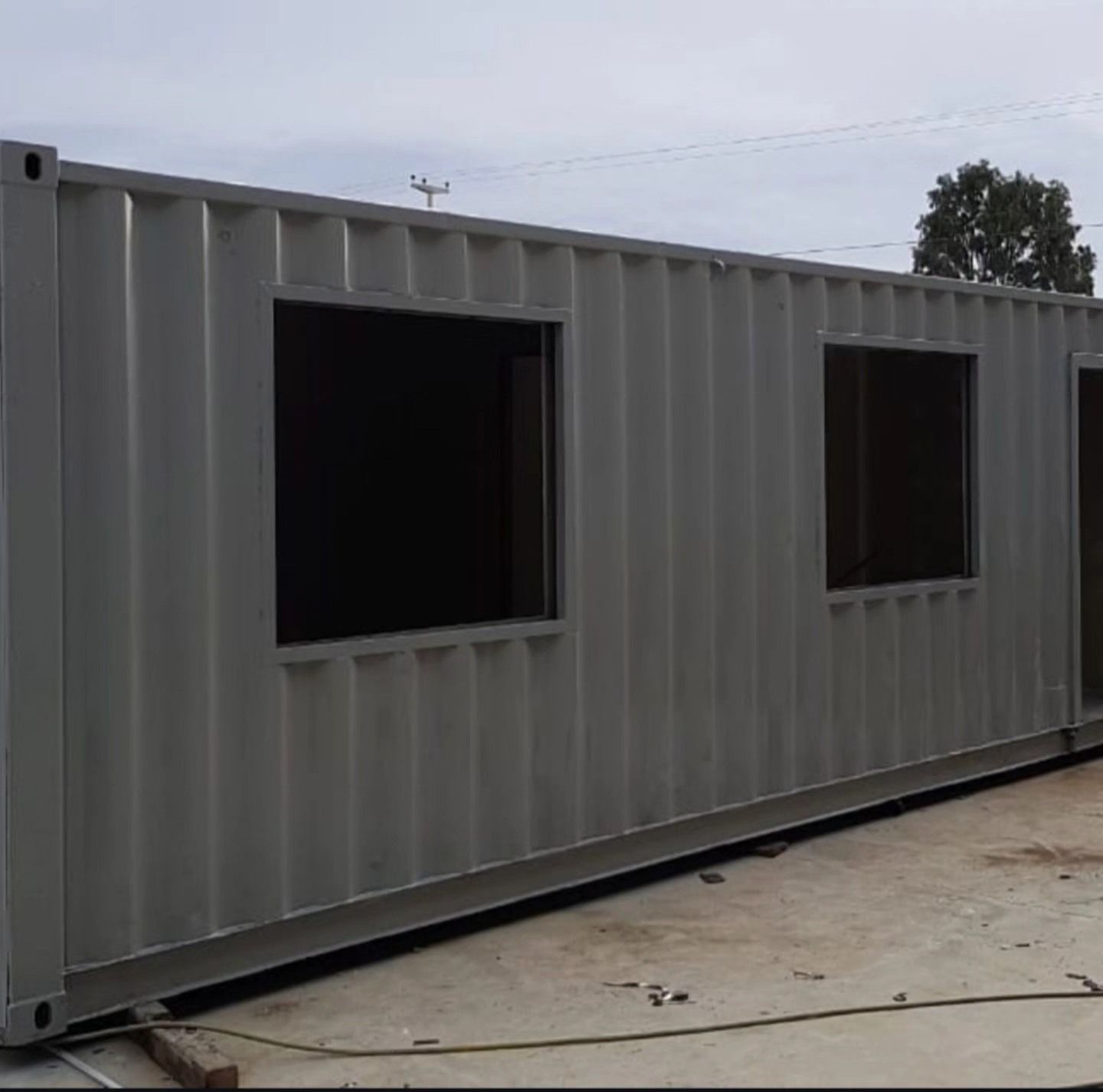 Un contenedor de envío gris con dos ventanas está en el suelo.