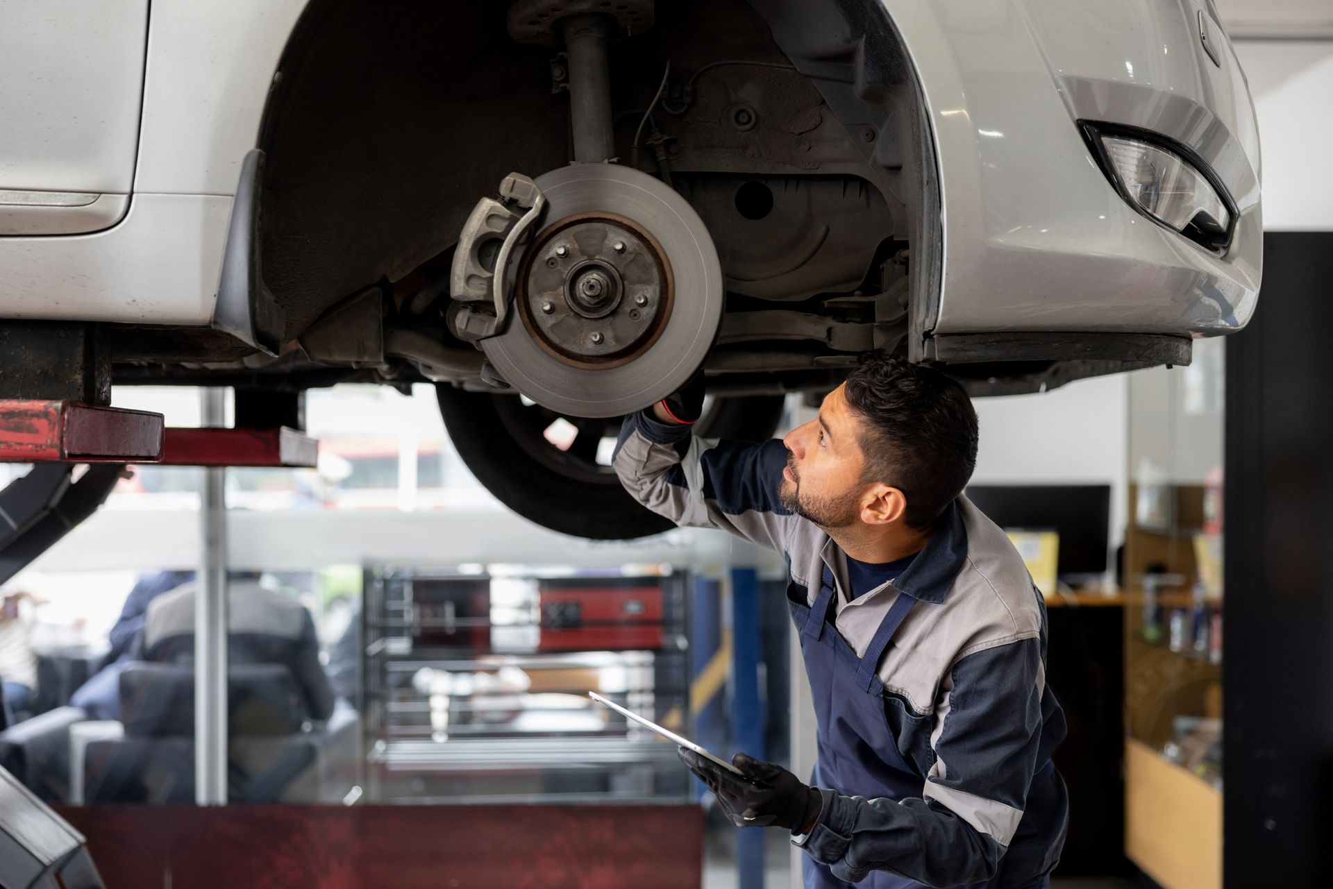 A male mechanic aligning a car tire at an auto repair shop and using a scanner.
