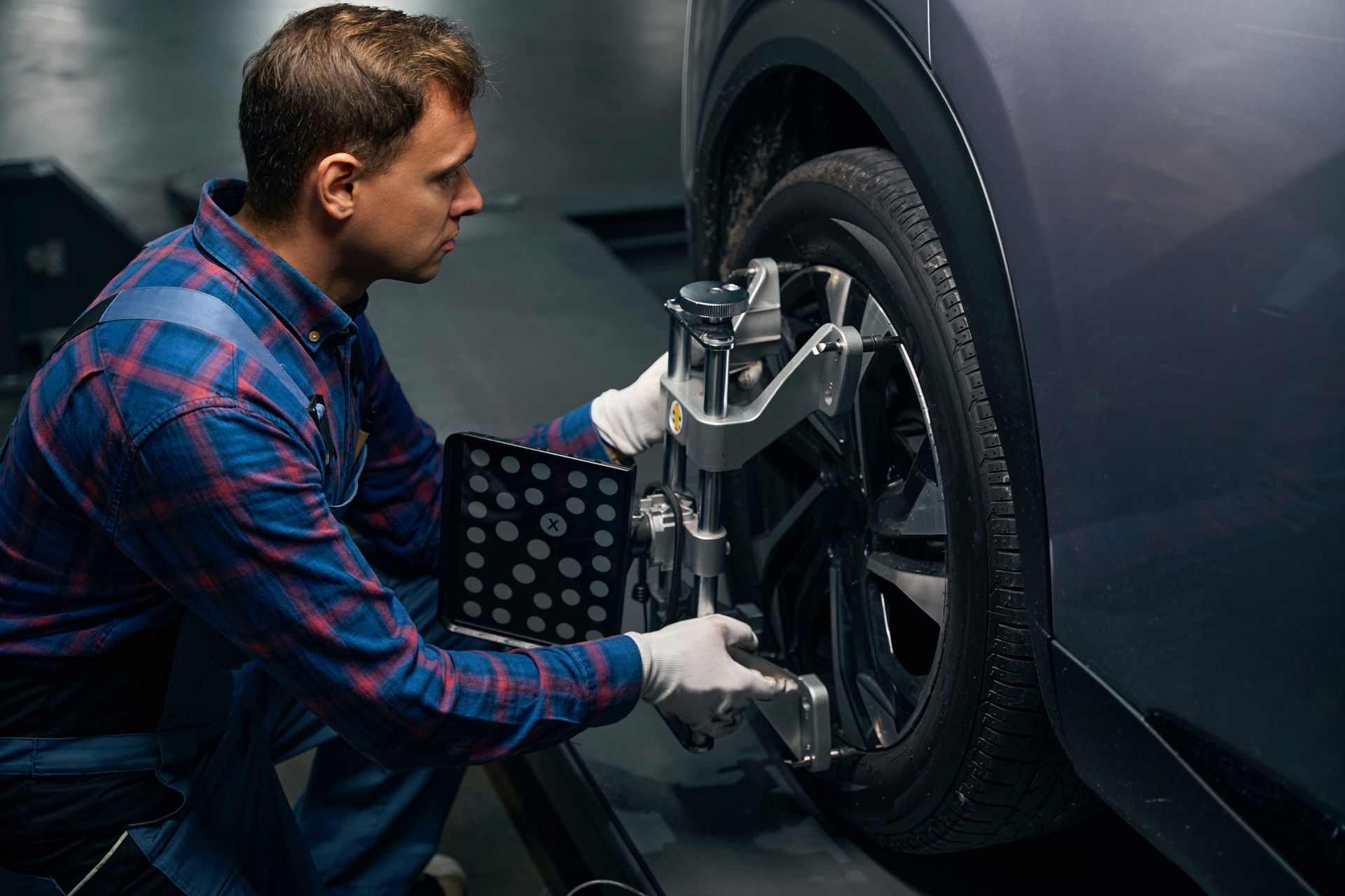 Mechanic adjusting car’s wheel alignment using a sensor device.