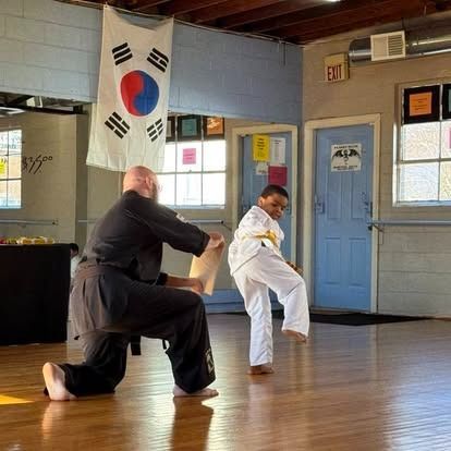A man and a boy are practicing martial arts in a room with a korean flag hanging from the ceiling.