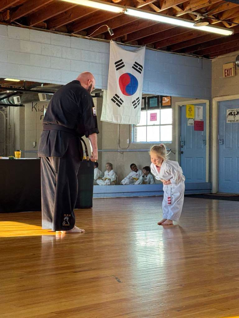 A man and a little girl are practicing martial arts in a gym.