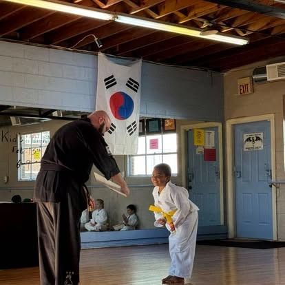 A man is teaching a young boy martial arts in a gym.