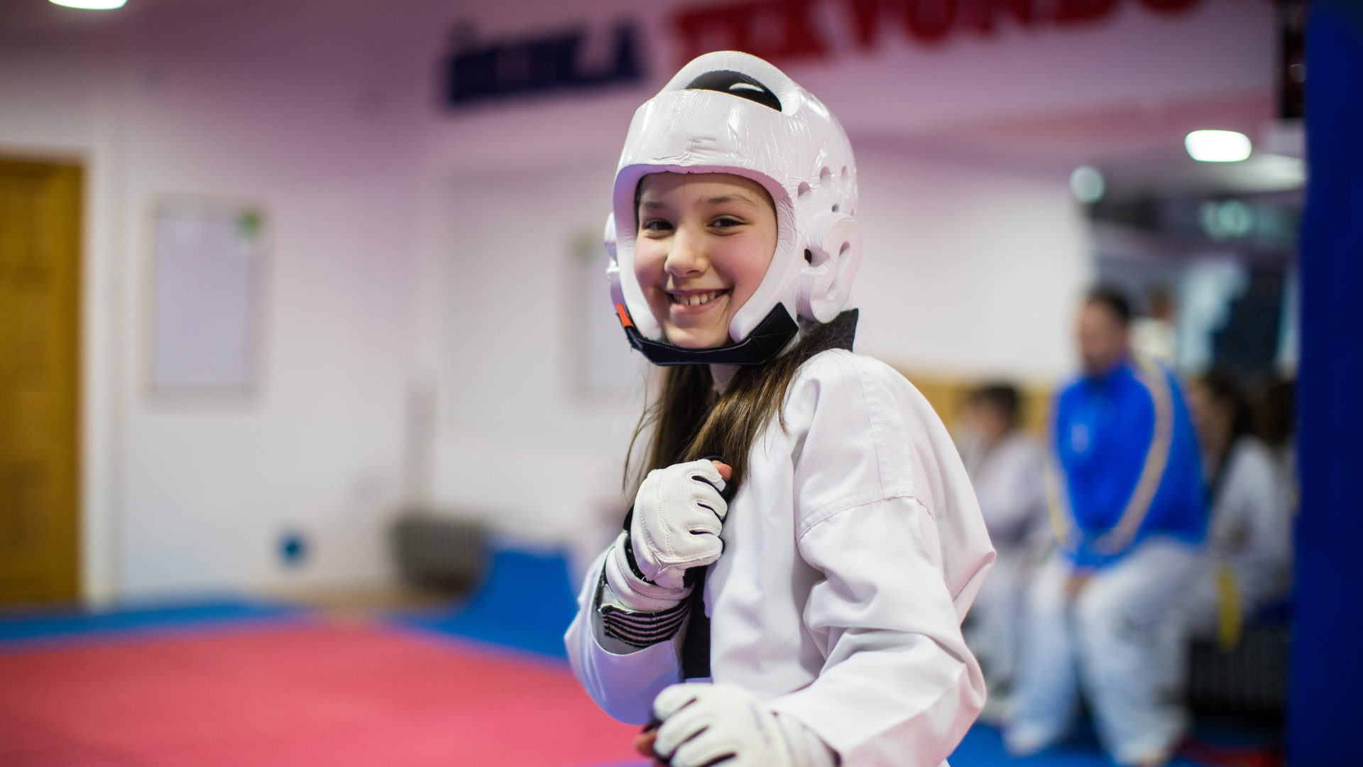A young girl is wearing a helmet and gloves while practicing taekwondo in a gym.