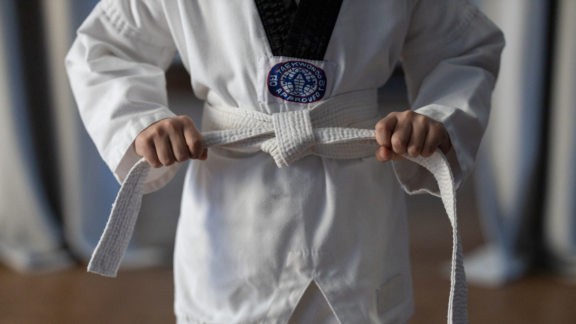 A young boy in a taekwondo uniform is tying his belt.