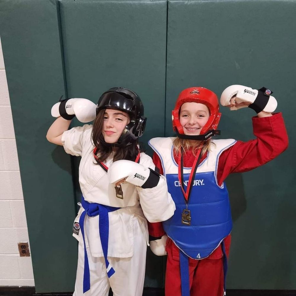 Two young girls are posing for a picture and one has a medal around her neck that says taekwondo