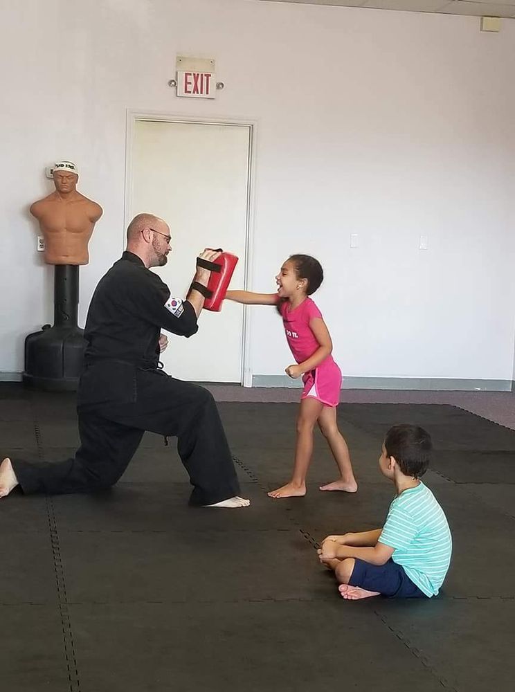 A man and two children are practicing martial arts in a gym.