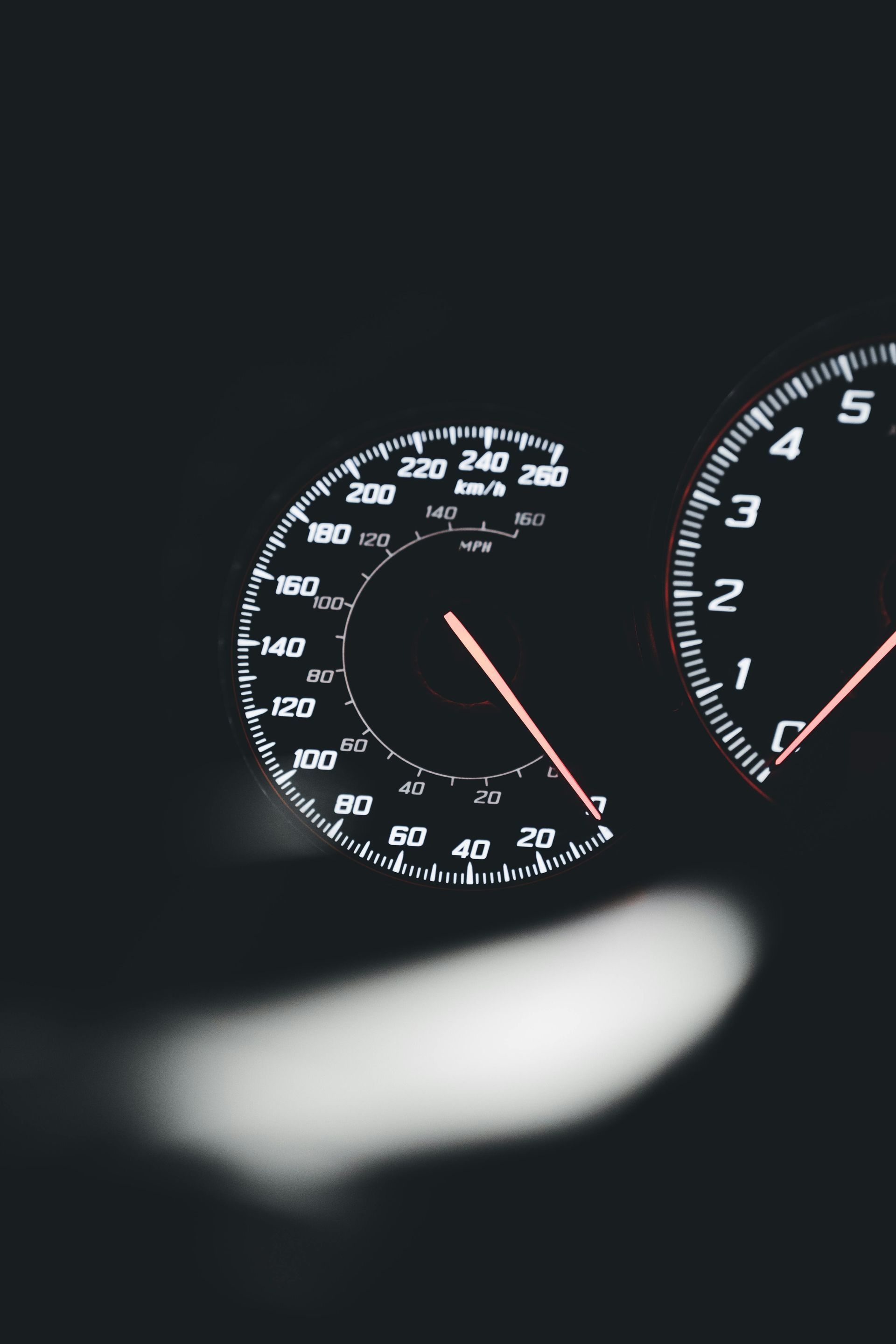 Car dashboard speedometer and tachometer glowing in the dark, with a blurred light in the foreground