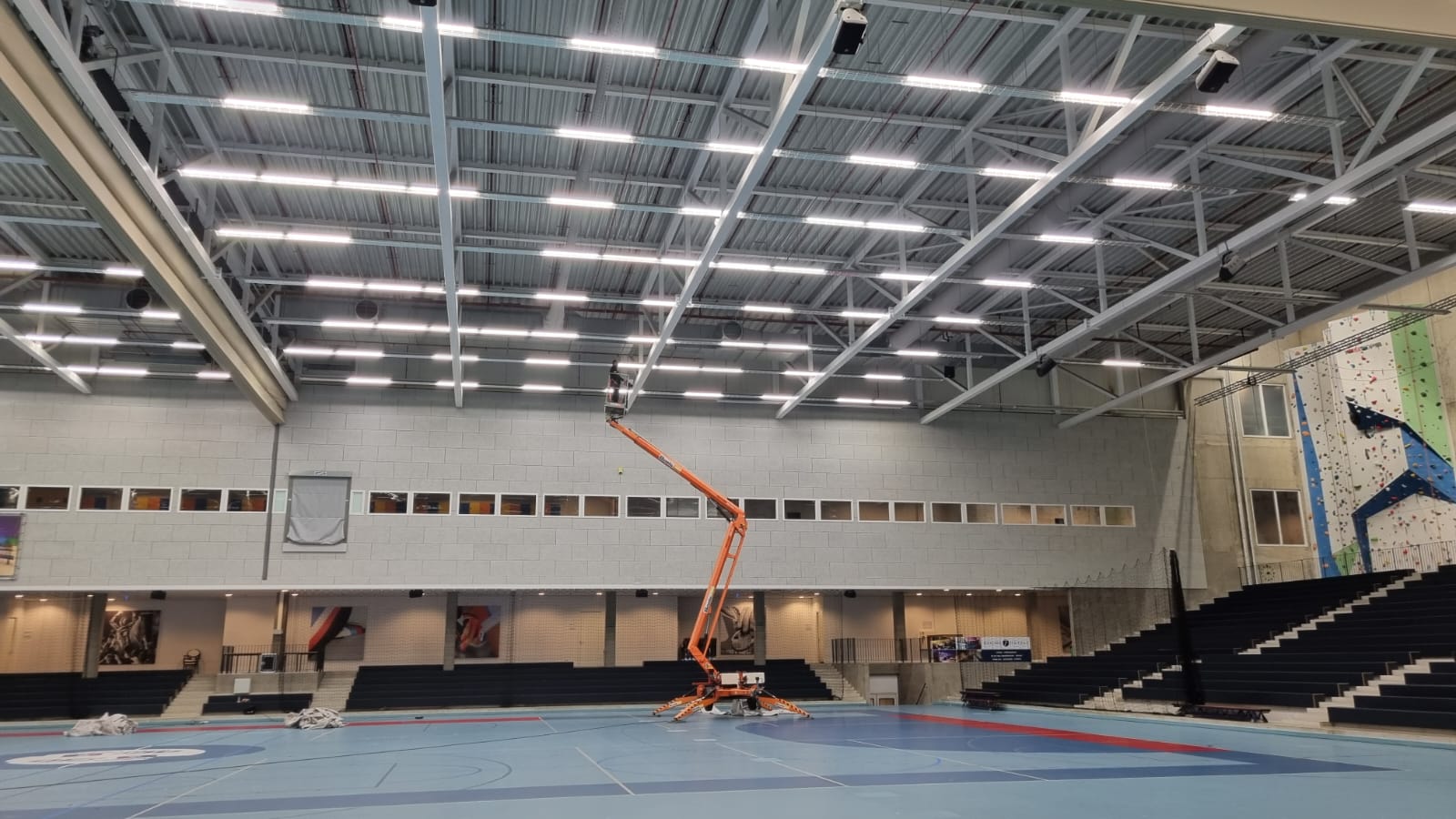 Een man gebruikt een kraan om airsocks/luchtverdeelslangen aan het plafond van een sportschool schoon te maken.