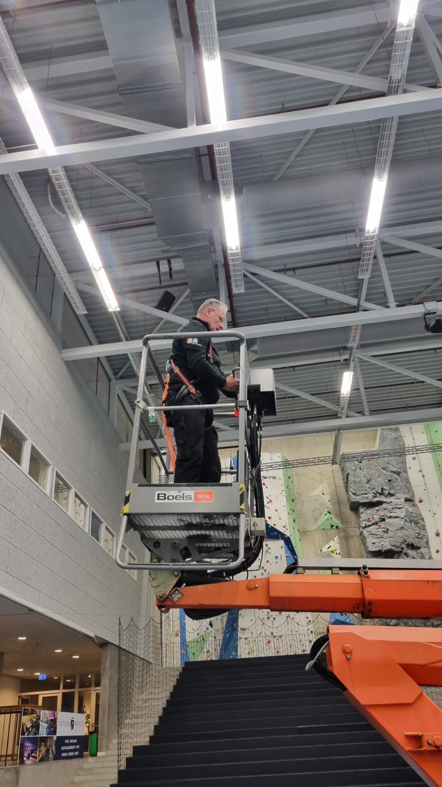 Een man werkt in een hoogwerker aan de airsock/luchtverdeelslang in een sporthal op grote hoogte.