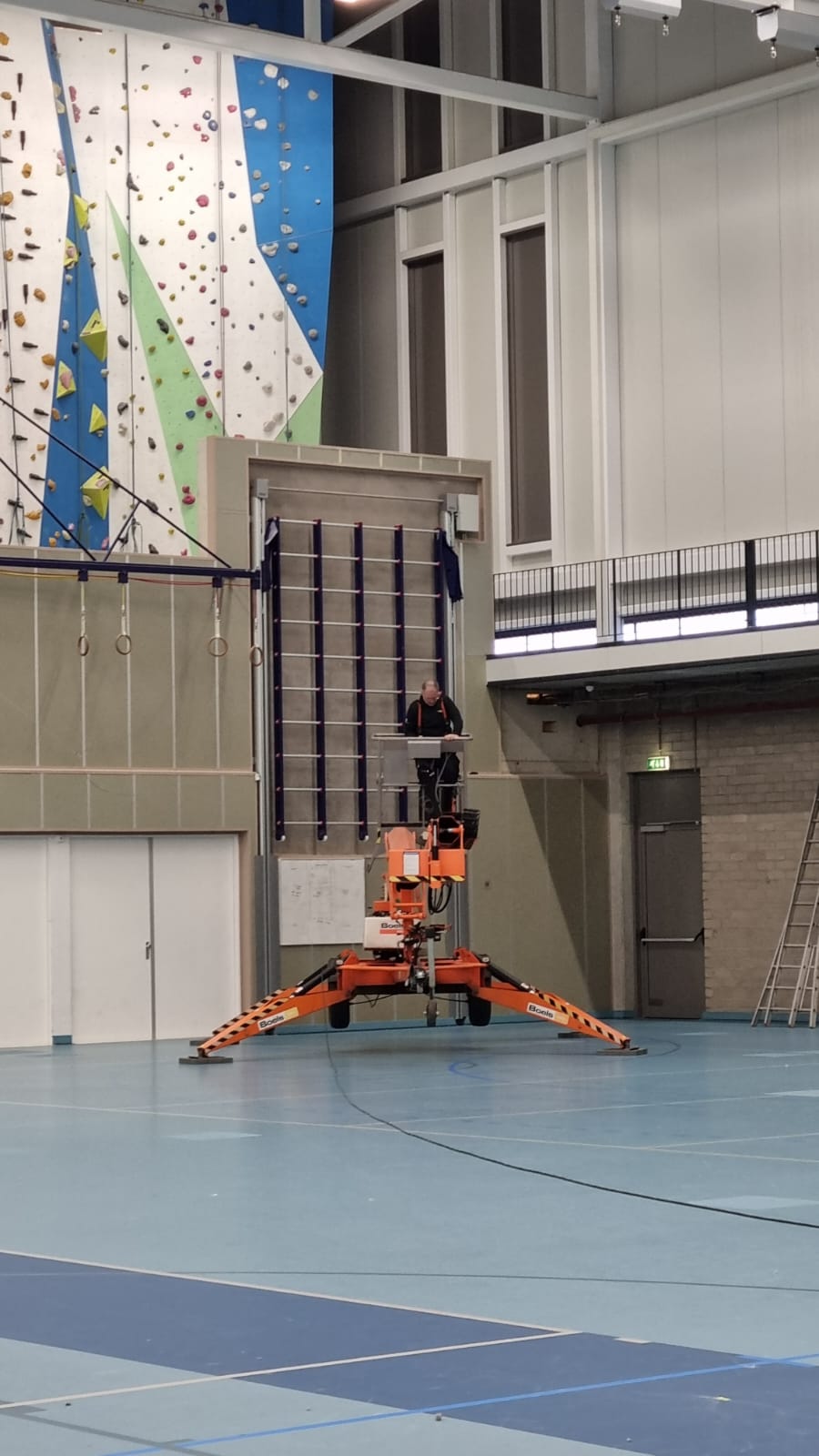 Een persoon staat op een hoogwerker in een sporthal.