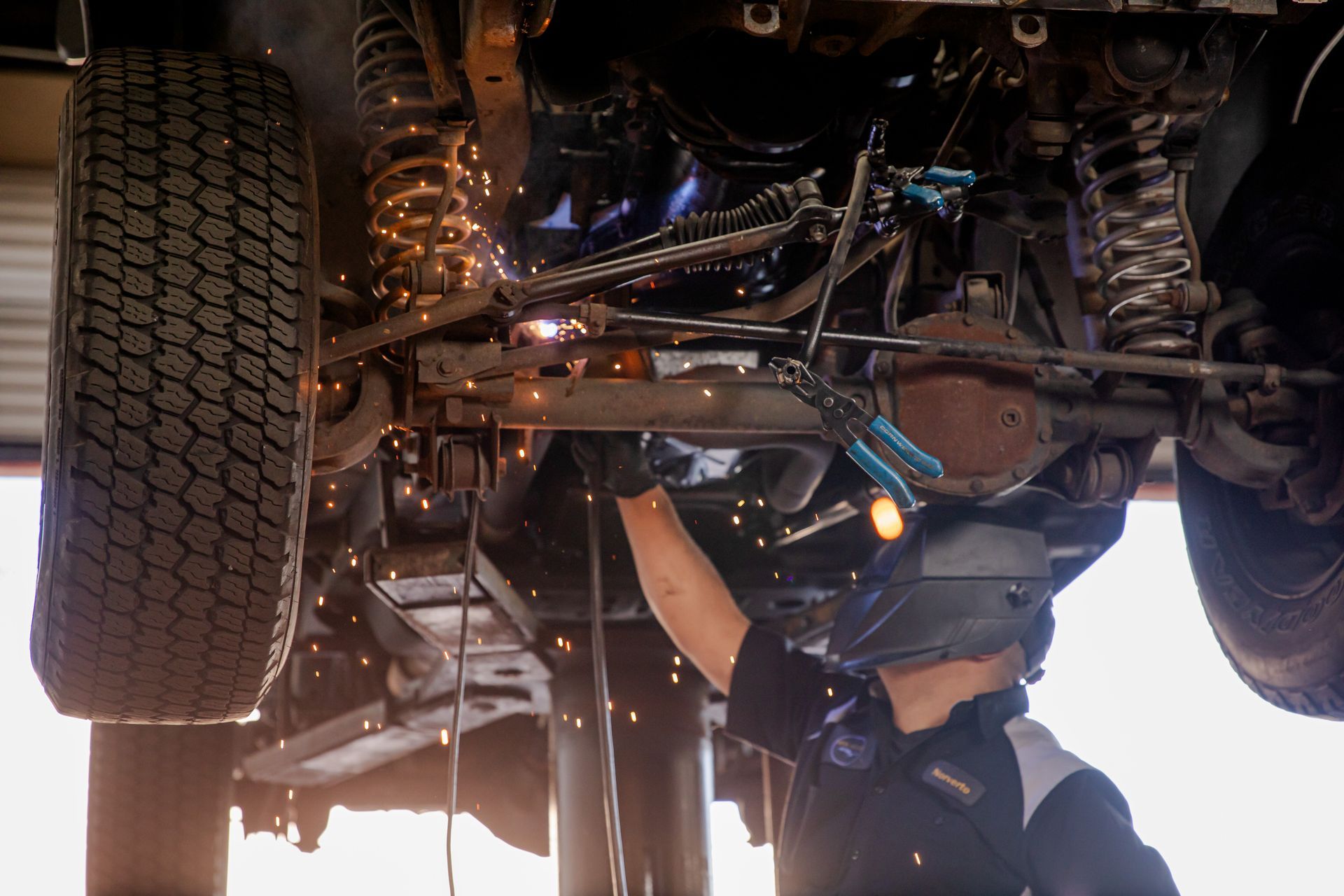 A man is welding underneath a car in a garage.