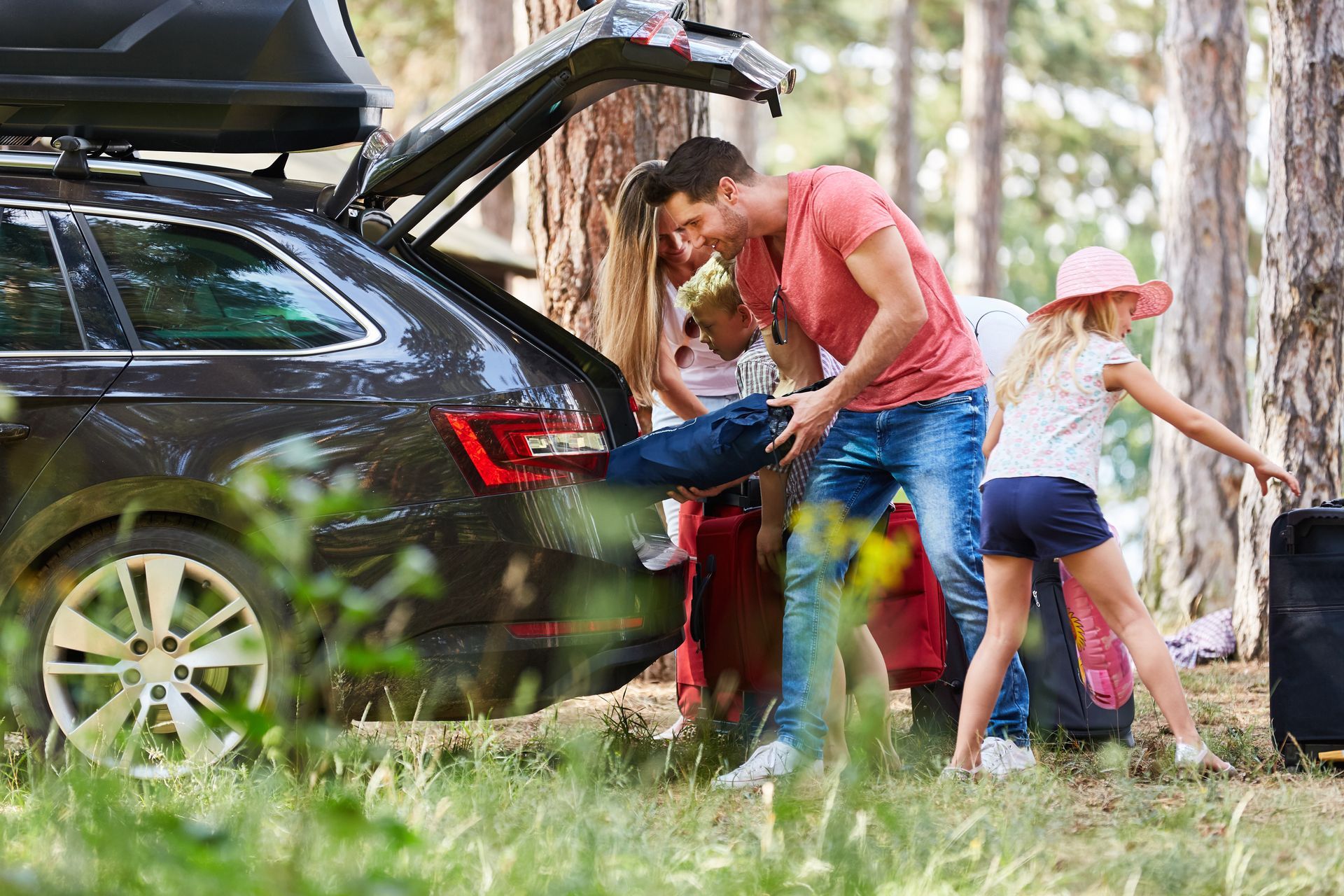 Family unloading luggage from car trunk in a forest.