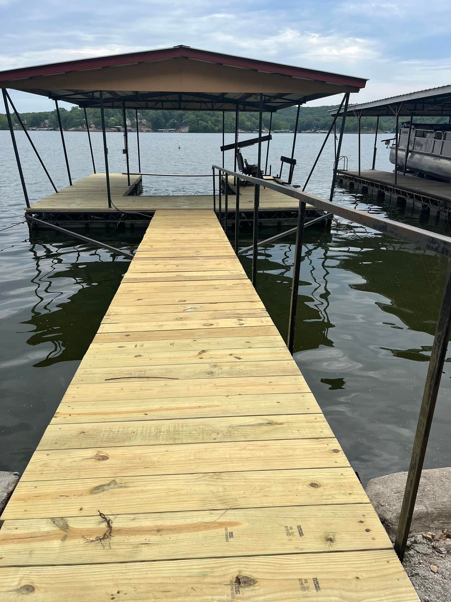 Wooden dock with a covered boat slip on a lake under a cloudy sky.
