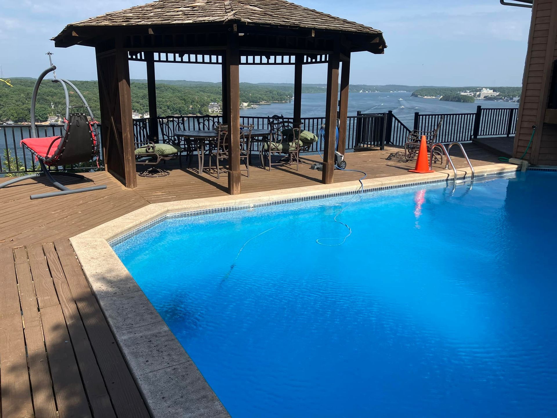 Swimming pool with gazebo overlooking a lake, wooden deck, blue water, and clear sky.