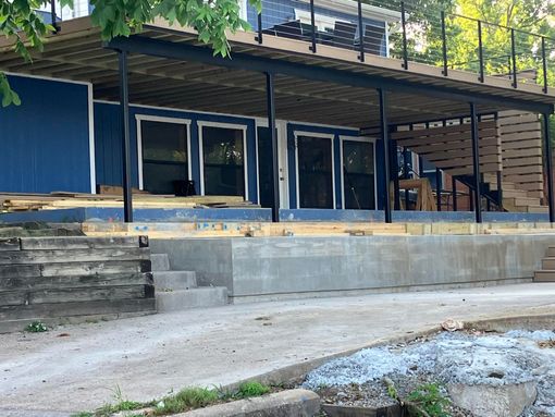 Blue house with elevated deck; concrete stairs and driveway in front.