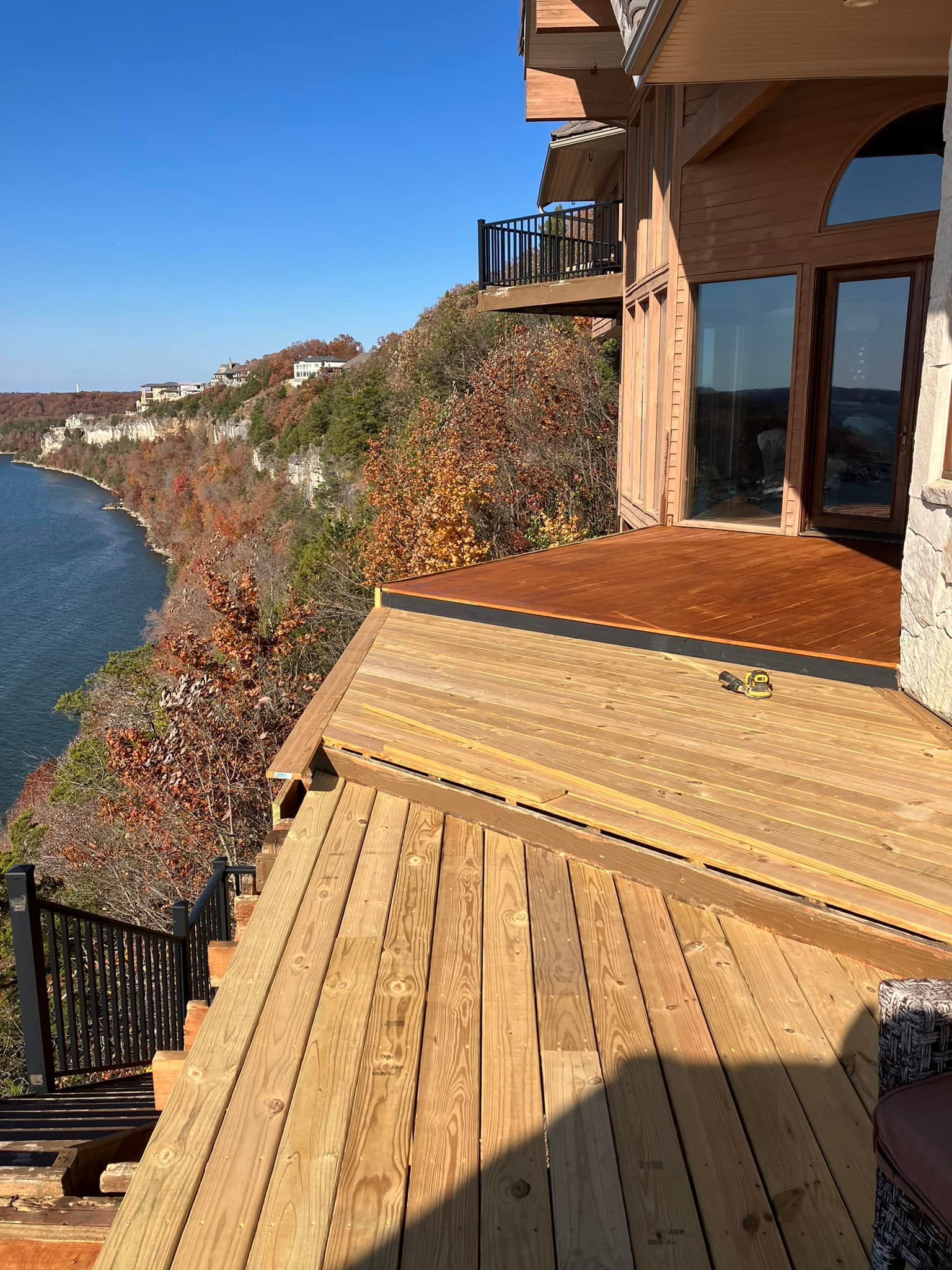 Wooden deck overlooking a lake and fall foliage. House with glass doors and stone facade.