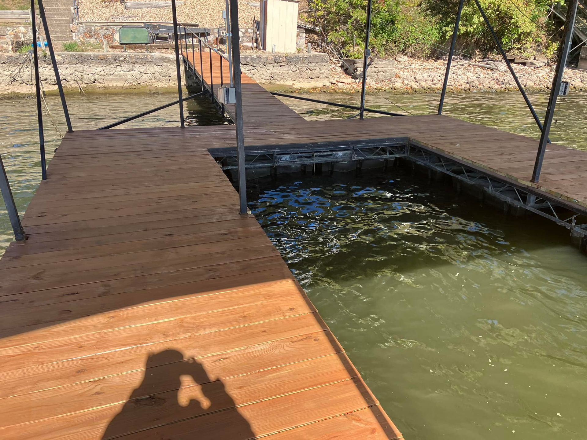 A dock with brown decking on a lake, containing a square cutout in the water.