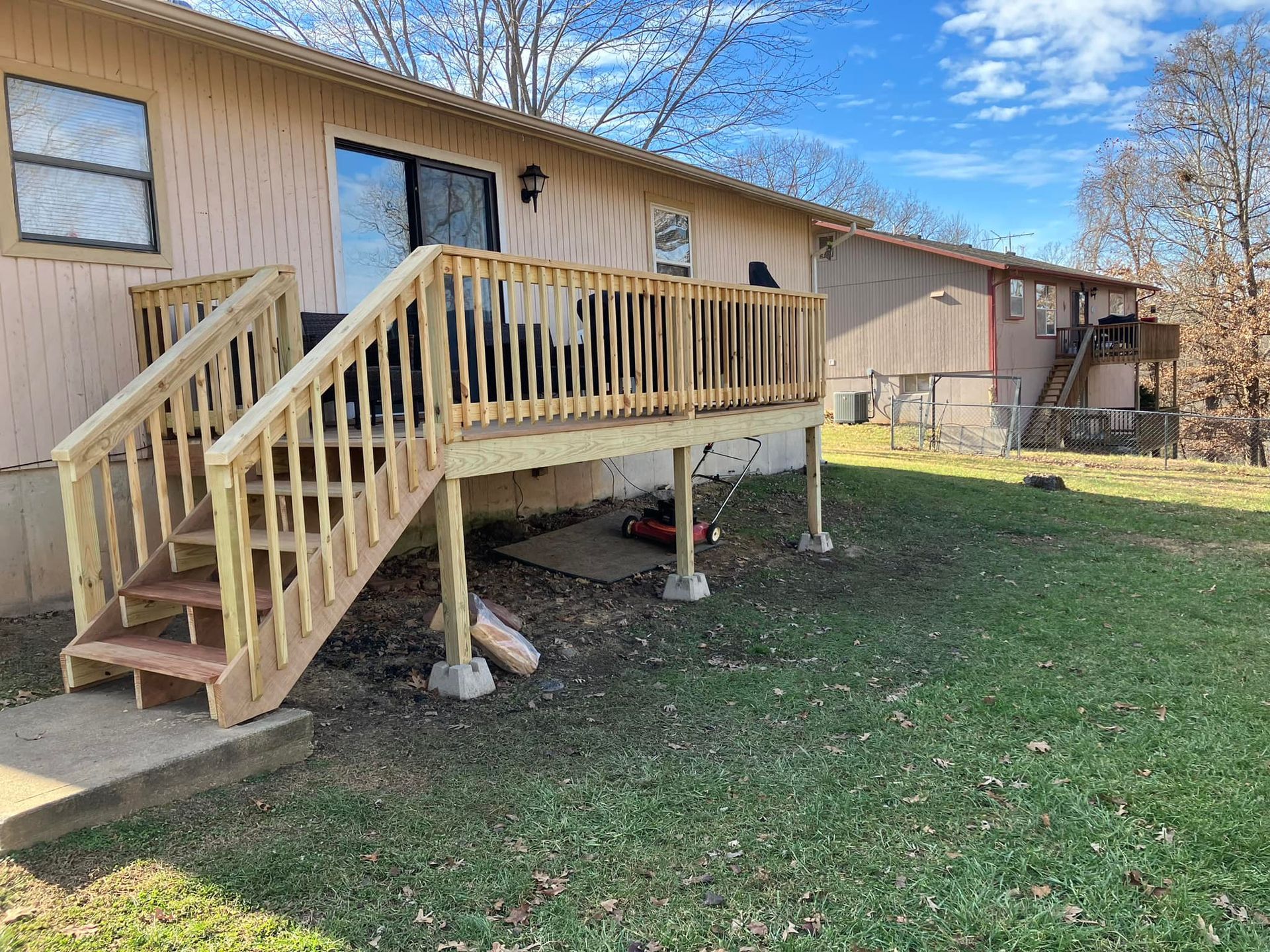 Wooden deck with stairs attached to a light beige house on a grassy lawn.