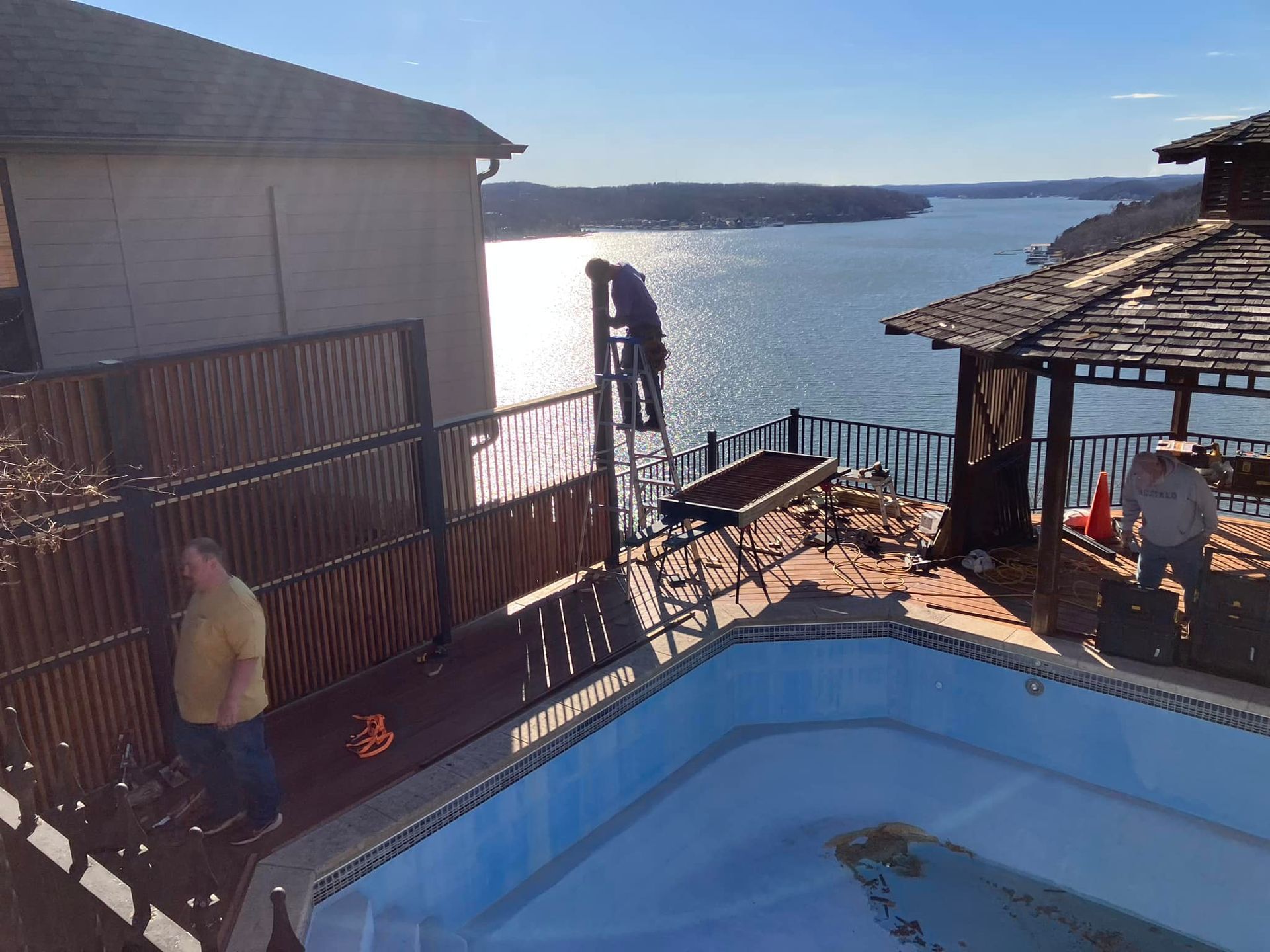 People working near a pool, building a fence overlooking a lake under a sunny sky.