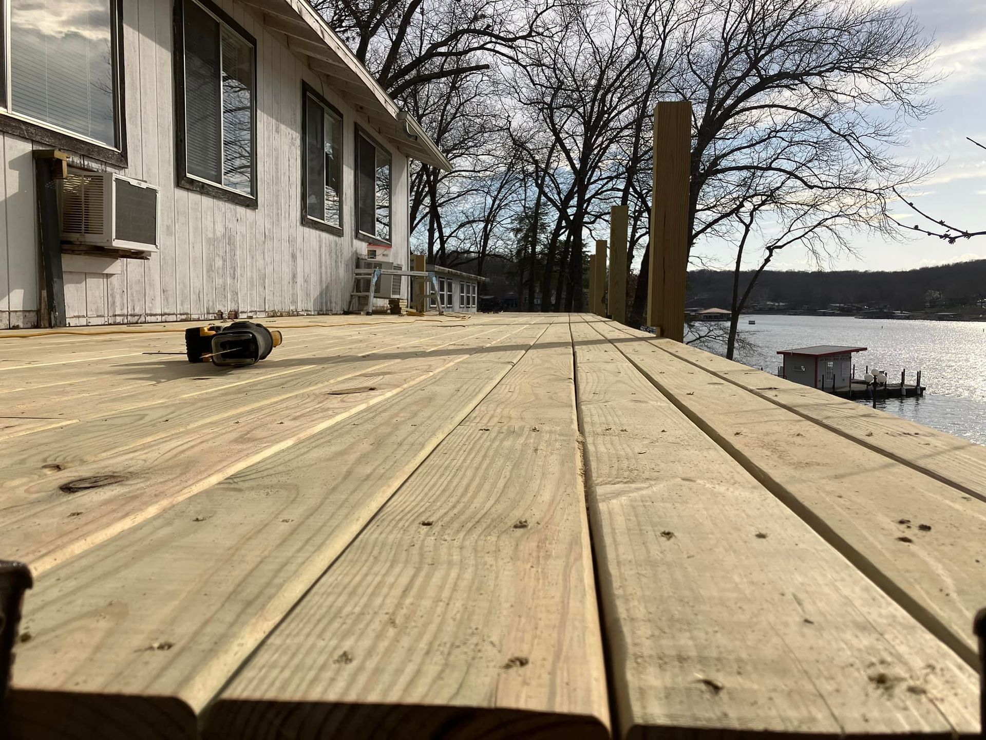 Wooden deck overlooking a lake, with a house on the left.