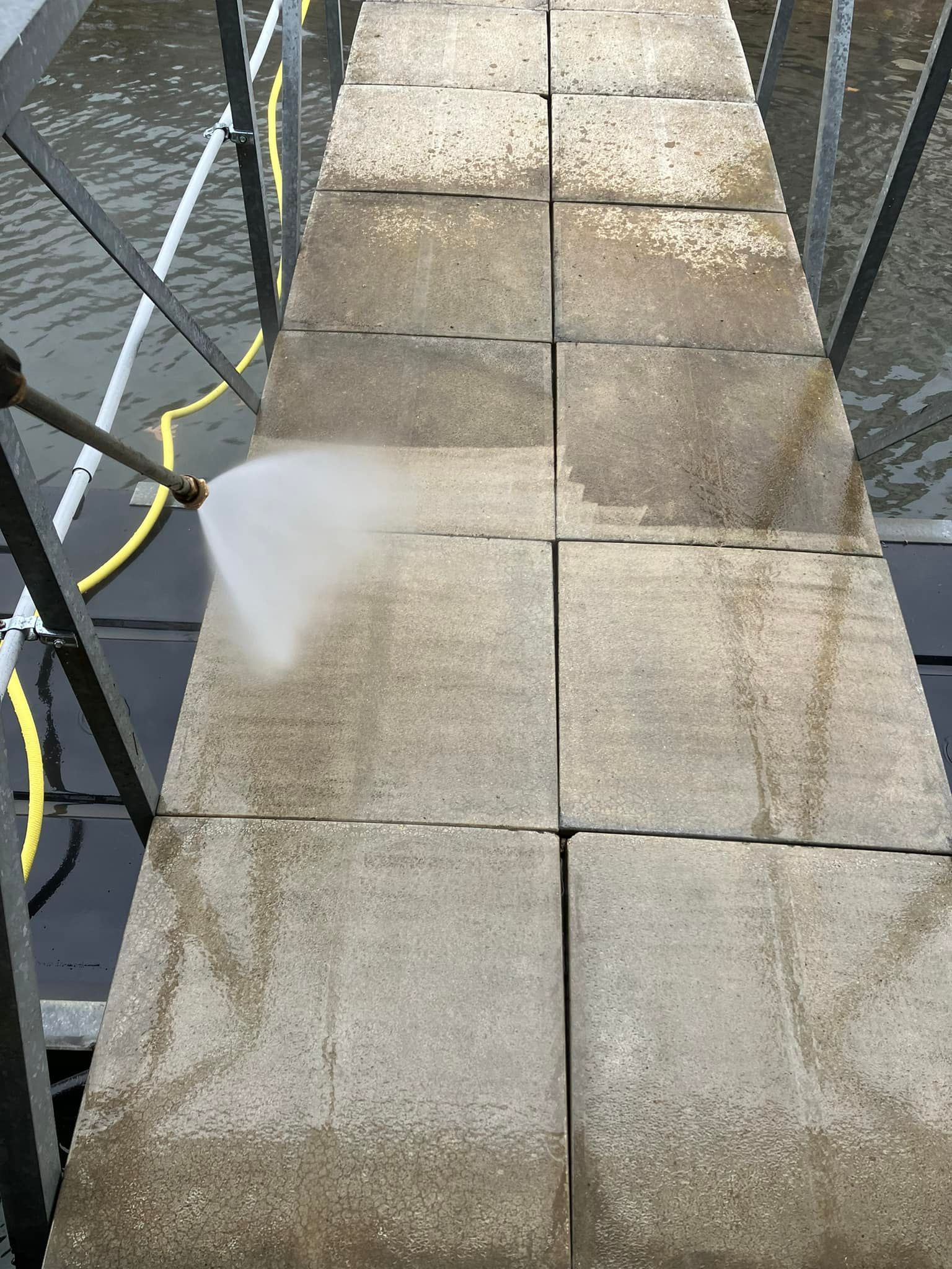 Pressure washing a stone walkway over water.