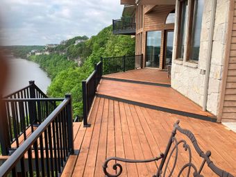 Wooden deck overlooking river and lush green hillside. Black railing and ornate bench.