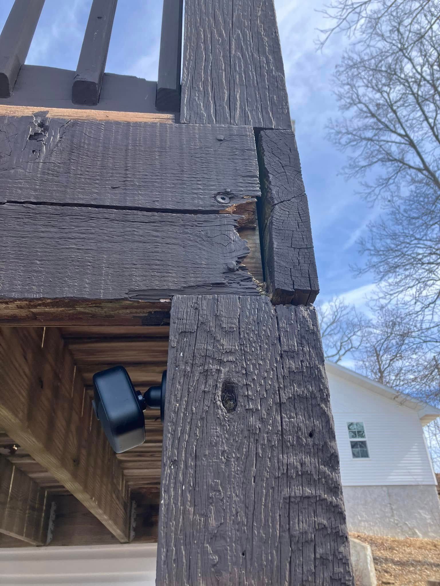 Black weathered wood deck post and railing corner. Sunlight and a house are in the background.