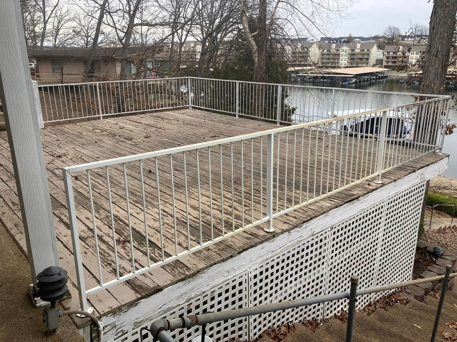 Wooden deck with white railing overlooking water, next to a house.