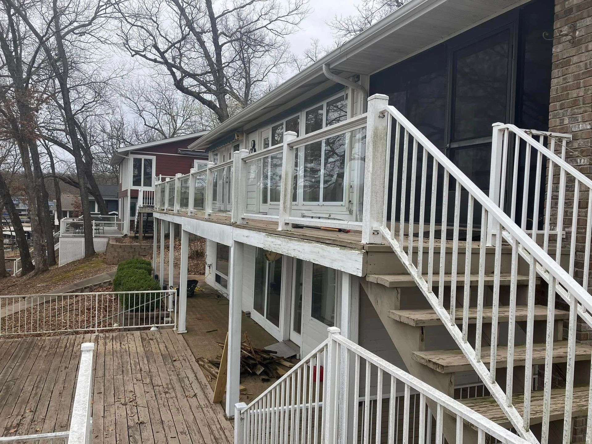 White lakeside house with glass railing, stairs, and a deck. Overcast day.