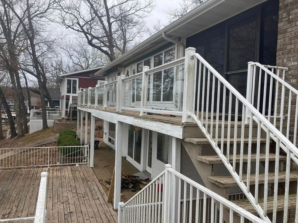 A two-story house with white railings and stairs leading to a wooden deck.