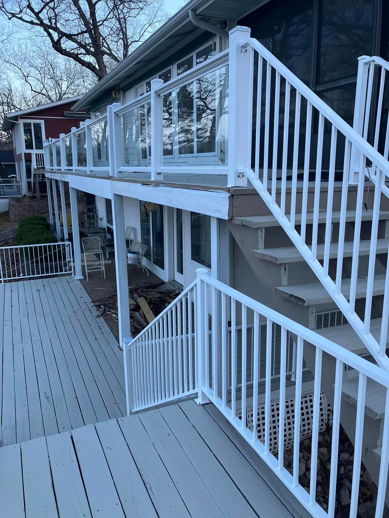 White deck and stairs on a house with glass panel railings, leading up to a higher level.