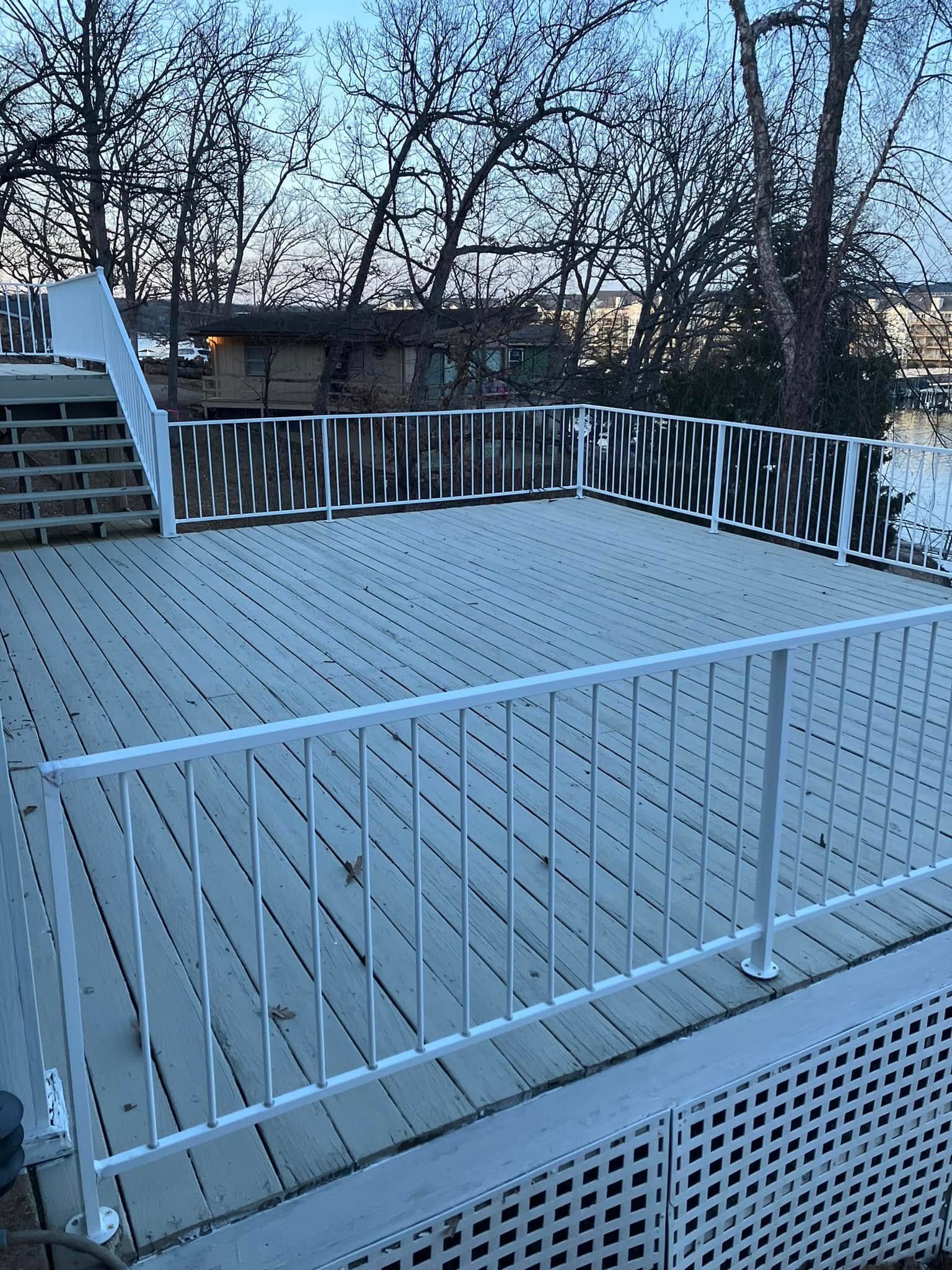White fenced deck, with stairs leading up, overlooking trees and a body of water.