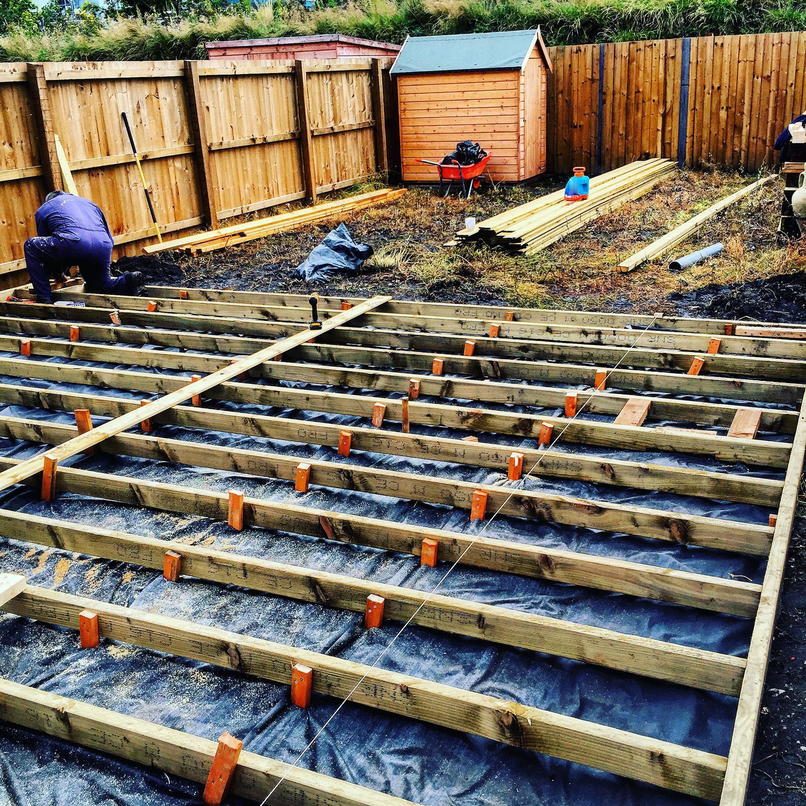 Deck under construction: planks removed, exposing wooden frame, next to a water body.