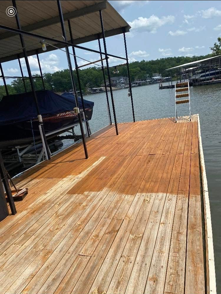 A person applying wood stain to a wooden deck with a paintbrush; brown stain, natural light.