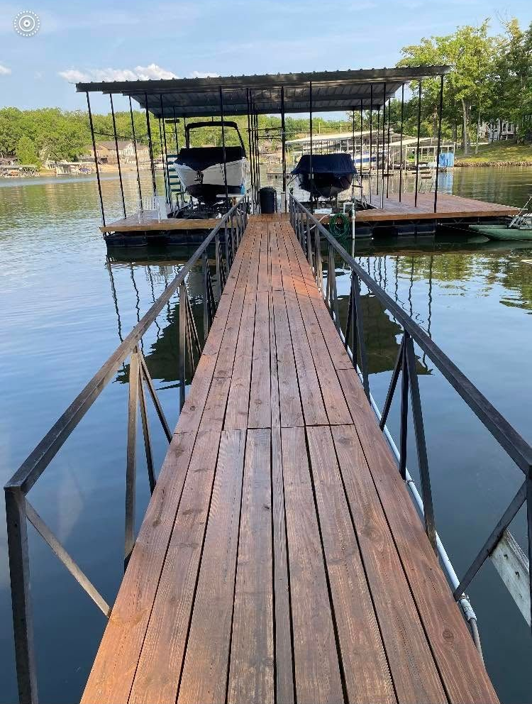 Wooden dock leads to a covered boat slip with two boats on calm water.