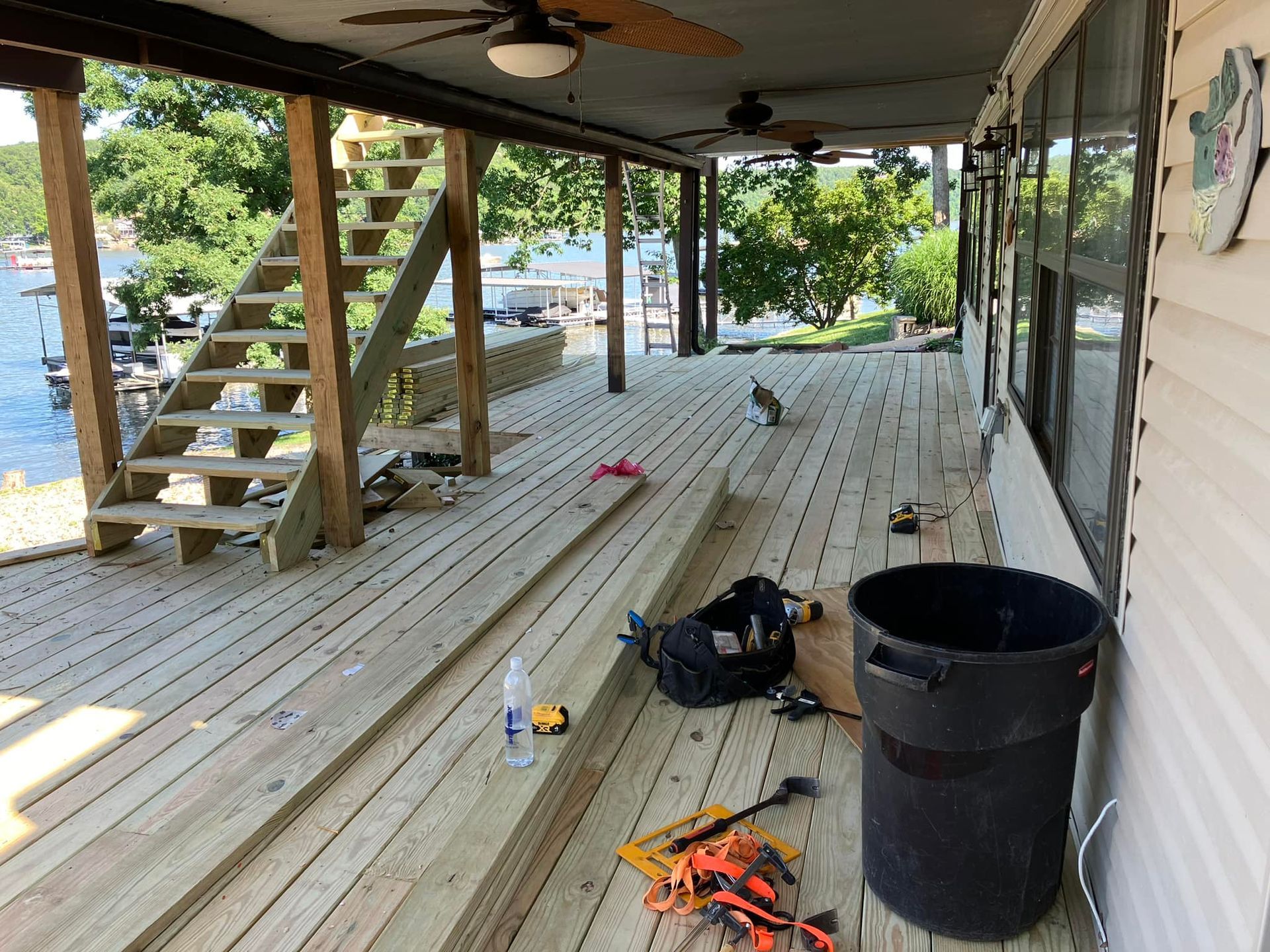 Deck with unfinished planks, tools, stairs, water view, and a trash can.