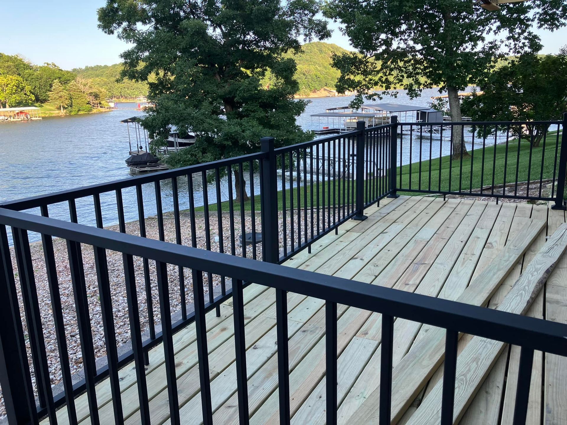 Black railing surrounds a wooden deck overlooking a lake, trees in the background.
