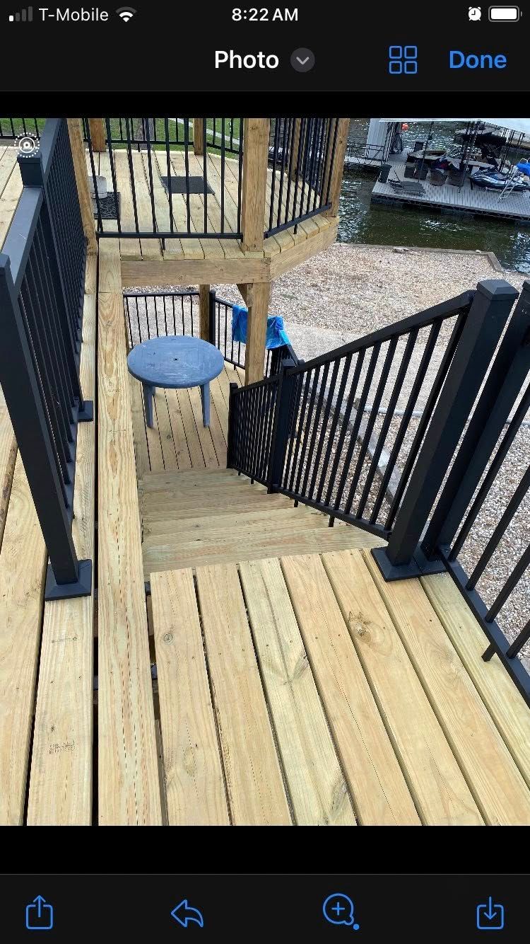 Wooden deck with black railing and staircase leading down to another level.