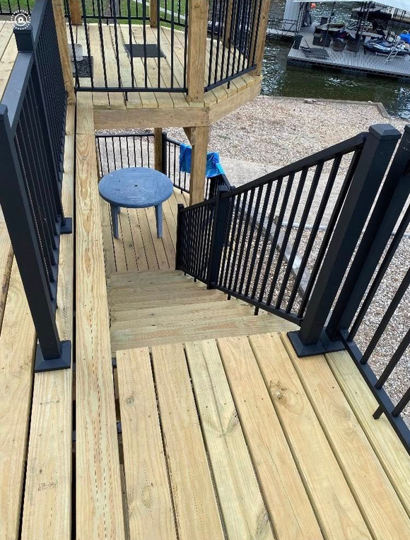 Wooden deck and stairs with black railings leading to a lower level, near a body of water.